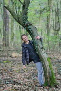 Portrait of woman standing by tree trunk in forest