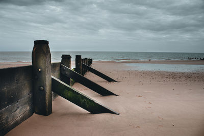 Wooden posts on beach against sky