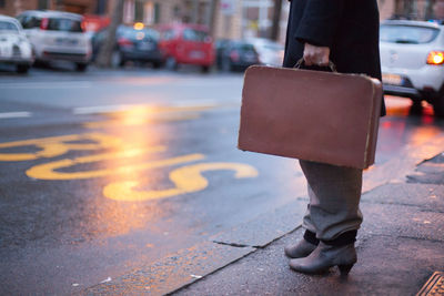 Low section of businesswoman standing on footpath by street