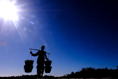 Silhouette man carrying baskets while standing against blue sky during sunny day