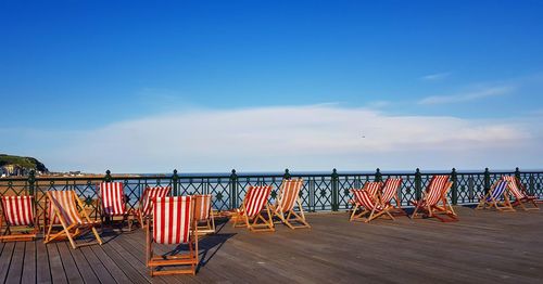 Empty chairs on beach against blue sky