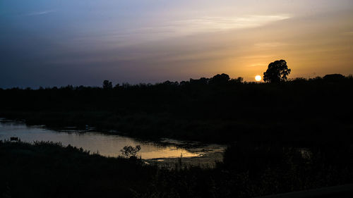 Silhouette trees on landscape against sky at sunset