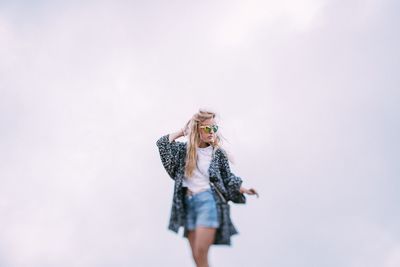 Young woman wearing sunglasses standing against sky