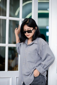 Portrait of young woman standing against window