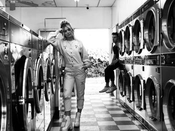 Full length portrait of young woman standing by washing machines