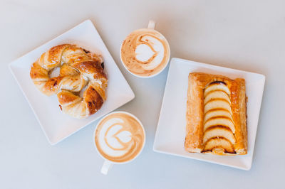 Directly above shot of snacks with cappuccinos served on table