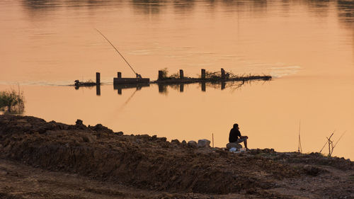 Man sitting against lake during sunset