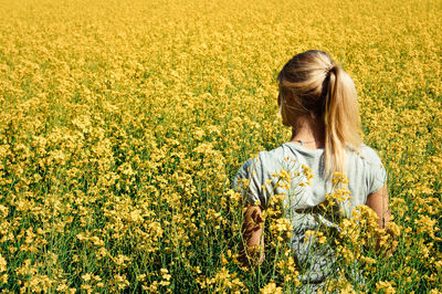 Rear view of young woman standing amidst oilseed rape