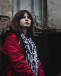 Young woman looking away while standing against wall