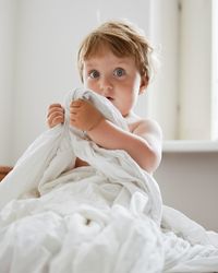 Portrait of cute baby boy holding blanket on bed at home