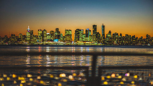 Illuminated modern buildings in city against clear sky