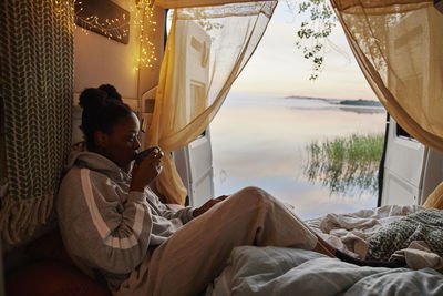 Woman sitting in bed in camper van and drinking tea