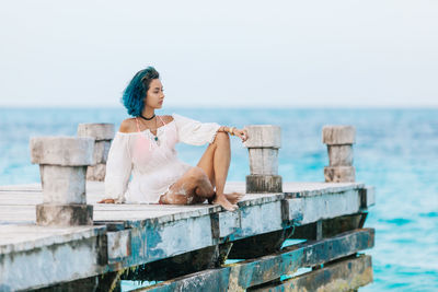 Full length of woman sitting on pier at beach against sky