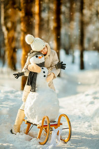 Girl embracing snowman on land during winter
