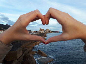 Cropped hands of woman making heart shape over sea