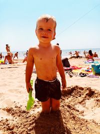 Portrait of shirtless boy standing in sand at beach against sky