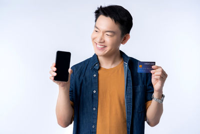 Smiling young man using smart phone standing against white background