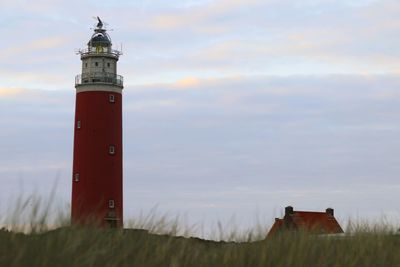 Lighthouse on field by building against sky