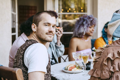 Portrait of smiling gay man with friends at dining table during dinner party in back yard