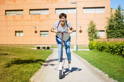 Full length of woman riding push scooter on footpath against building