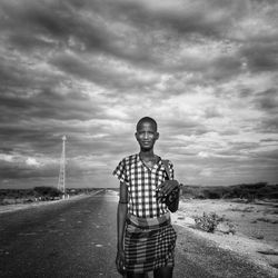Portrait of man standing on road against cloudy sky