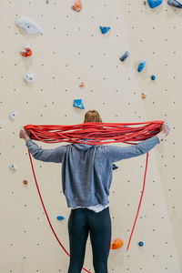 Back view of sportive female with ropes for climbing behind back standing near wall during training in gym