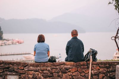 Rear view of people sitting on retaining wall by lake