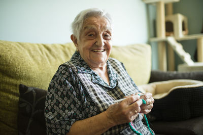 Portrait of smiling senior woman crocheting on the couch at home
