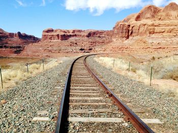 Railroad tracks leading towards mountains against sky