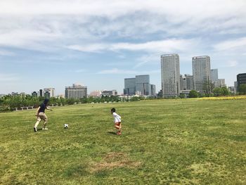 People playing soccer on field in city against sky