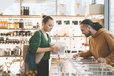 Man reading labels on counter by woman with container in shop