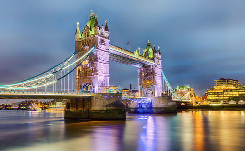 Tower bridge over thames river against cloudy sky in city at dusk