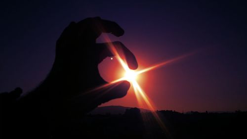 Close-up of hand holding sun during sunset