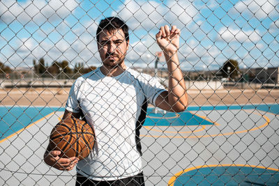 Full length of young man standing by chainlink fence