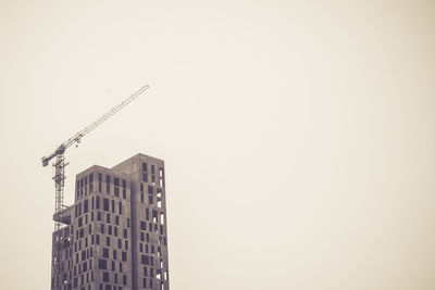 Low angle view of crane by building against clear sky