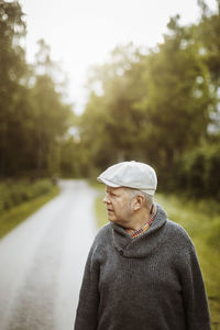 Mature man looking away while standing on road against trees