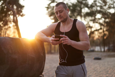 Young man holding camera while standing by tree