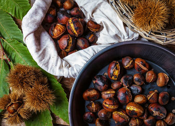 Top view of roasted chestnuts in iron skillet on wooden table.