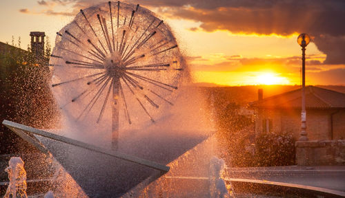 Ferris wheel by building against sky during sunset