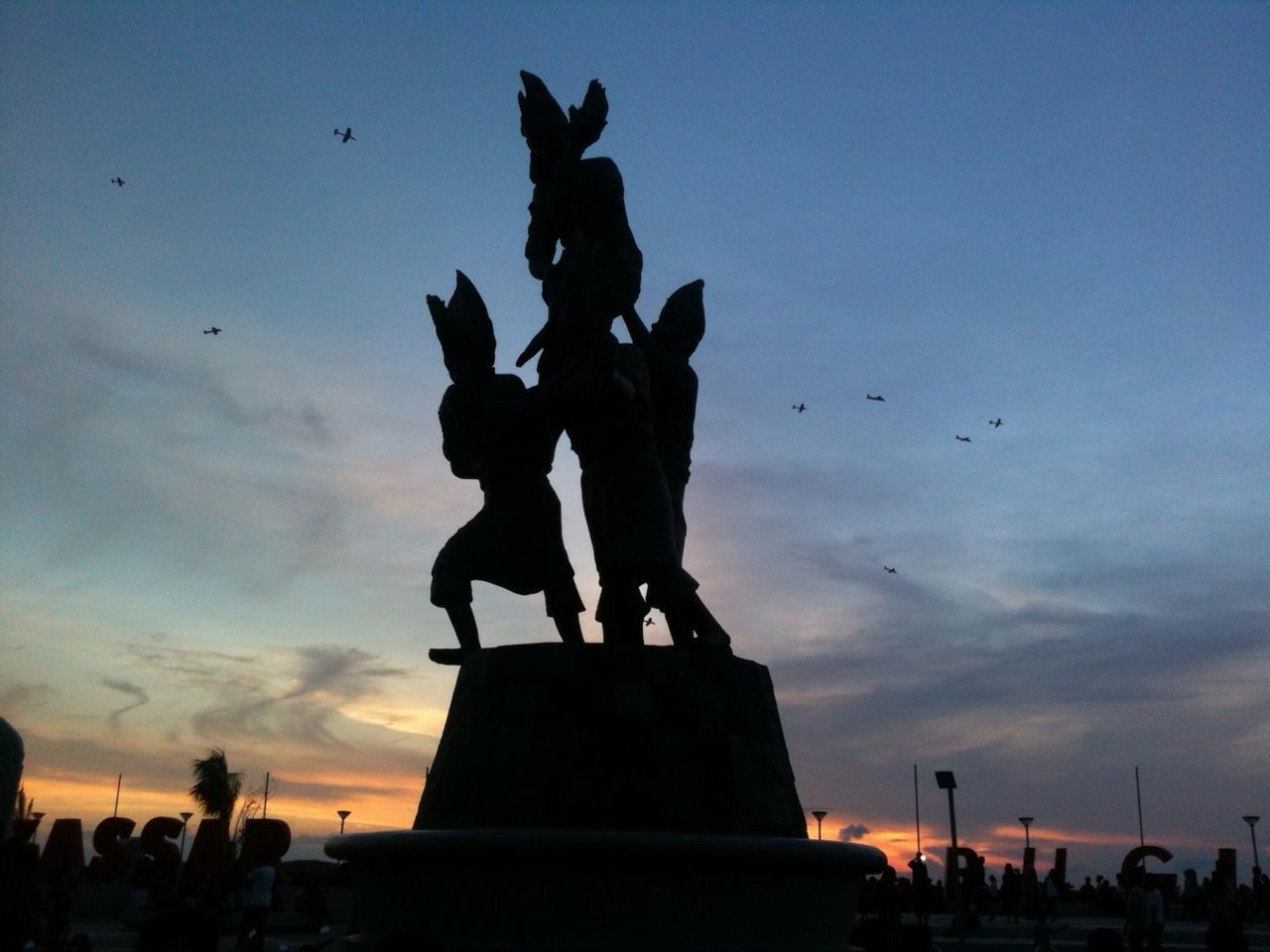 statue, sculpture, human representation, art and craft, art, silhouette, sky, creativity, bird, low angle view, sunset, cloud - sky, flock of birds, architecture, animal representation, built structure, monument, travel