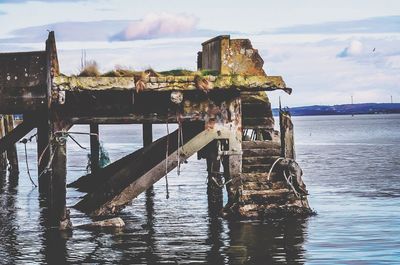 Wooden posts in sea against sky