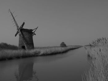 Traditional windmill by canal against clear sky