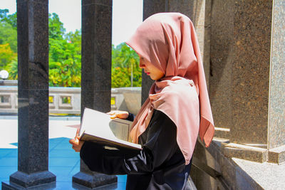 Young woman reading holy book while standing at mosque