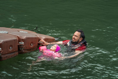 High angle view of father and daughter swimming in lake