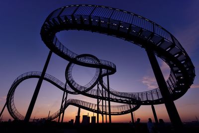 Low angle view of rollercoaster against sky at sunset