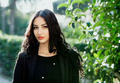 Portrait of beautiful young woman standing against plants