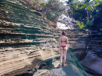 Rear view of bikini woman standing on rock formation