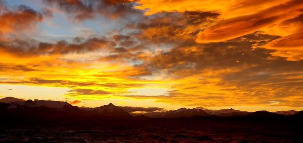 Scenic view of dramatic sky over silhouette landscape during sunset