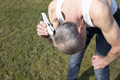 A gray-haired middle-aged man shaves his hair with a clipper in a garden