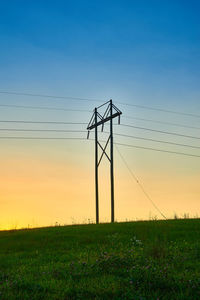 Silhouette electricity pylon on field against sky during sunset